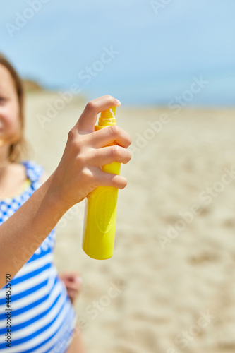 Little girl in swimsuit hold in hand yellow bottle of sunscreen standing on the beach