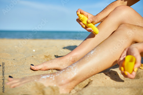 Woman sitting on the sandy beach, putting suncream on her skin © bondarillia