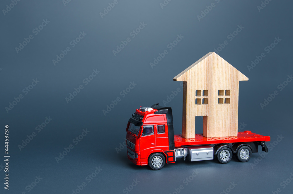 Fototapeta premium Red truck transports the residence house. Delivery services to another house. A moving company. Transportation of real estate. Resettlement program for new housing. Building insurance.