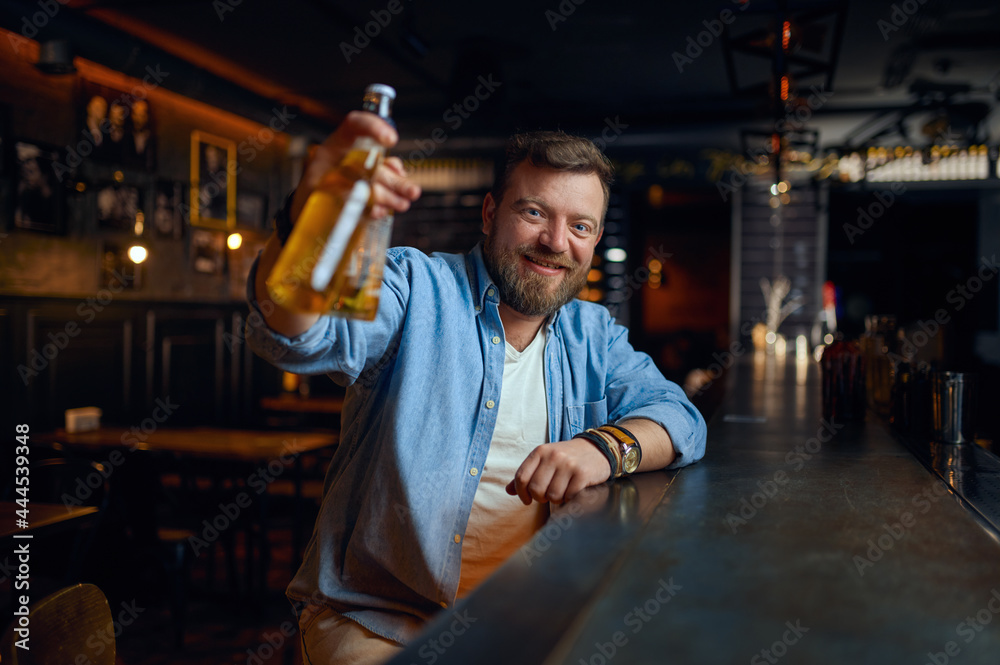 Smiling man with bottle of beer at counter in bar