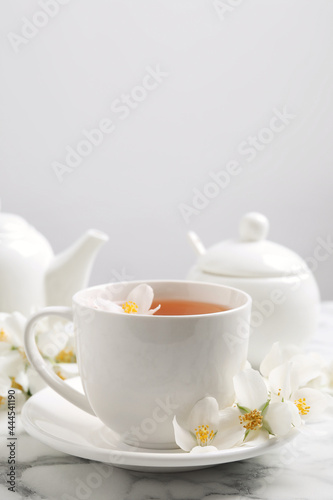 Aromatic jasmine tea and fresh flowers on white marble table, space for text