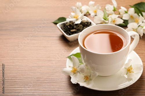 Cup of aromatic jasmine tea and fresh flowers on wooden table, space for text