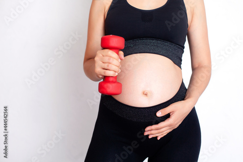 A pregnant woman in a sports uniform holds a dumbbell in her hands. Sports during pregnancy. close-up. White background. A place for text.