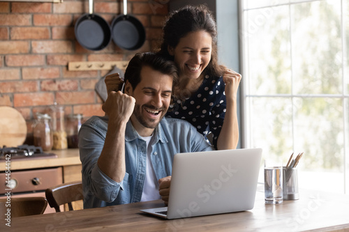 Happy excited young couple making winner yes hand fist gesture at laptop, getting awesome news, celebrating achieve, success, winning prize, getting unexpected income. Good surprise concept