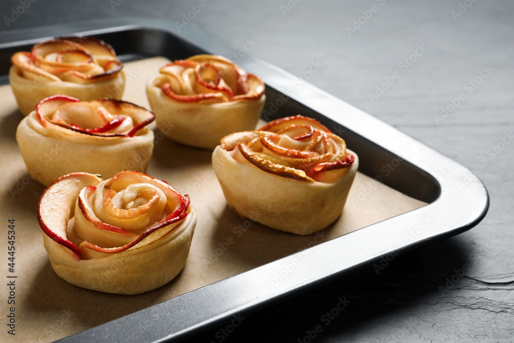 Tray with freshly baked apple roses on black table, closeup. Beautiful dessert