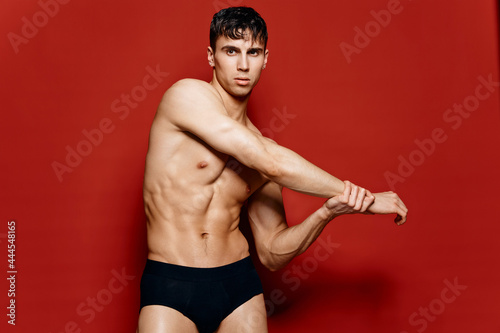 young guy athlete with an inflated torso and arm muscles pose on a red background