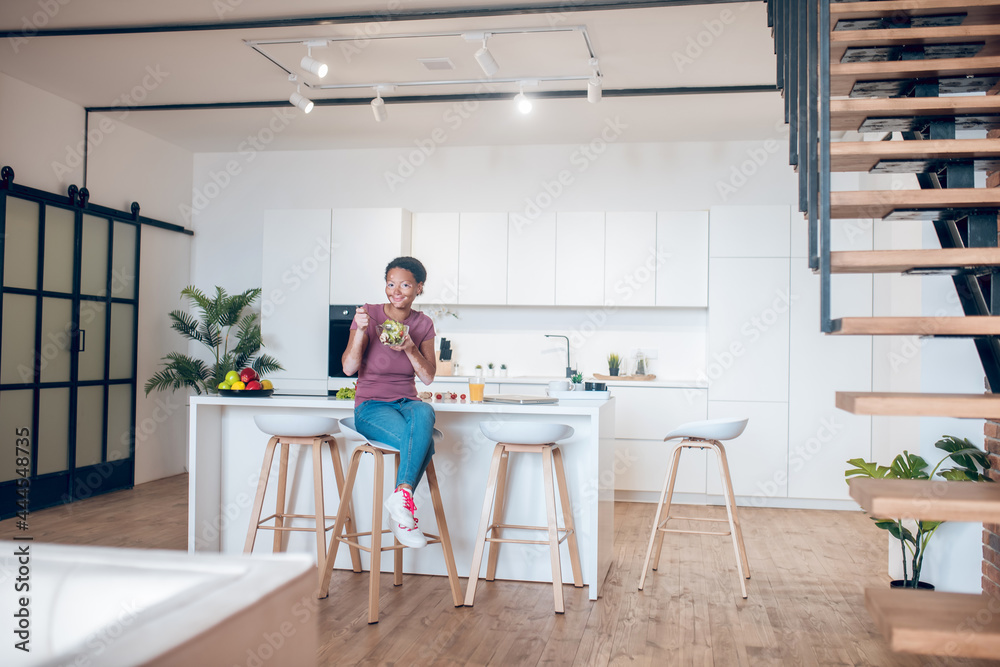 Fototapeta premium A dark-skinned woman sitting in the kitchen and eating salad