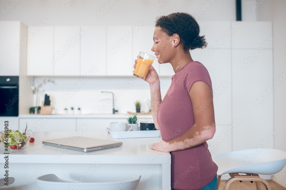 A dark-skinned woman drinking an orange juice