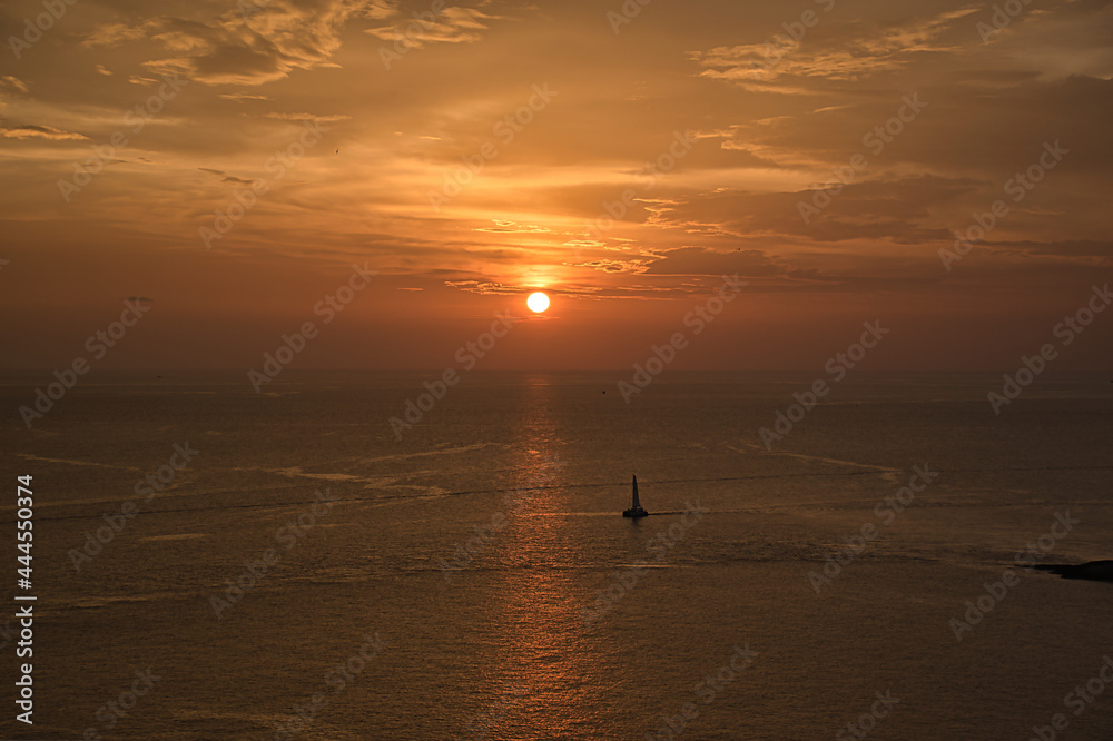 Beautiful, stunning panoramic view of the golden sky and reflections on the Andaman sea with sailing boats during the sunset at Promthep Cape landmark viewpoint in Phuket