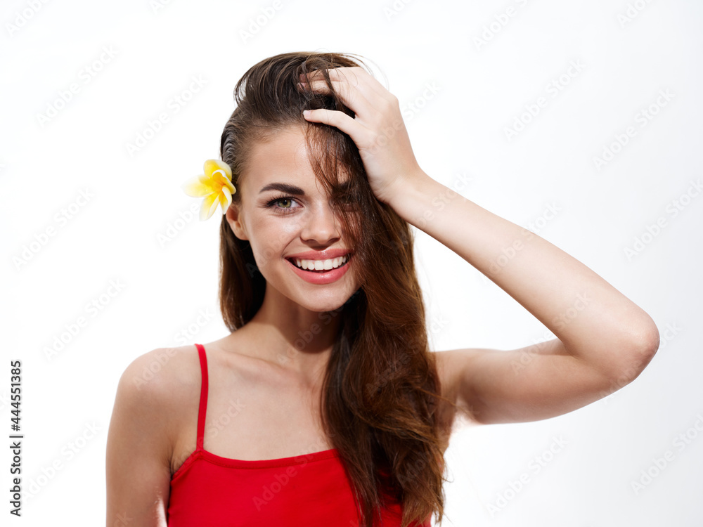 joyful brunette woman with a flower in her hair touches her head with her hand