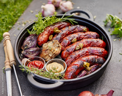 Grilled pork sausages and vegetables served with ketchup and mustard in a cast iron dish