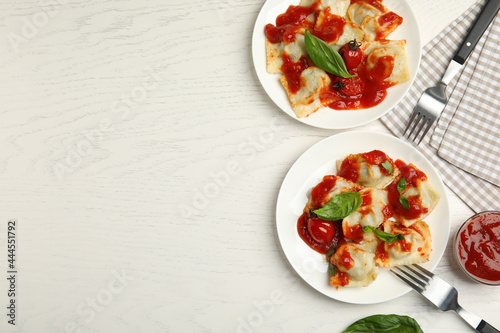 Tasty ravioli with tomato sauce served on white wooden table, flat lay. Space for text