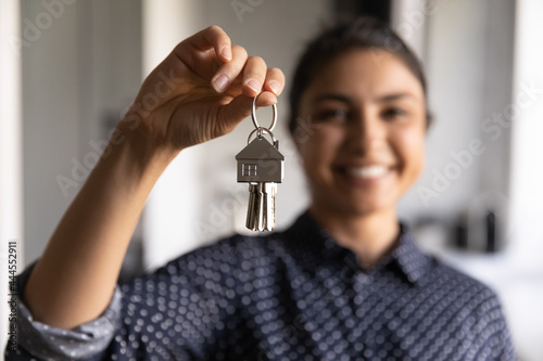 Happy Indian woman ready to move into new home. Real estate agent offering rent or buying house, flat, apartment, help with loan and mortgage. Hand of buyer or home owner holding key. Closeup