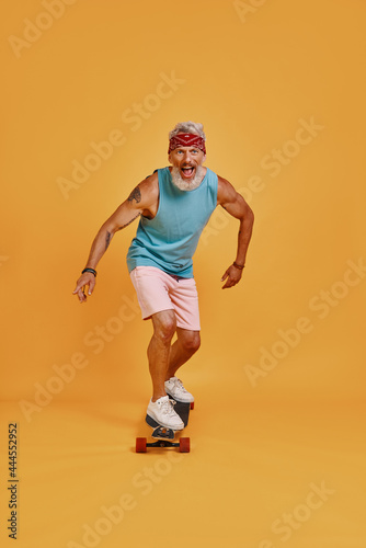 Full length of active senior man skateboarding against orange background