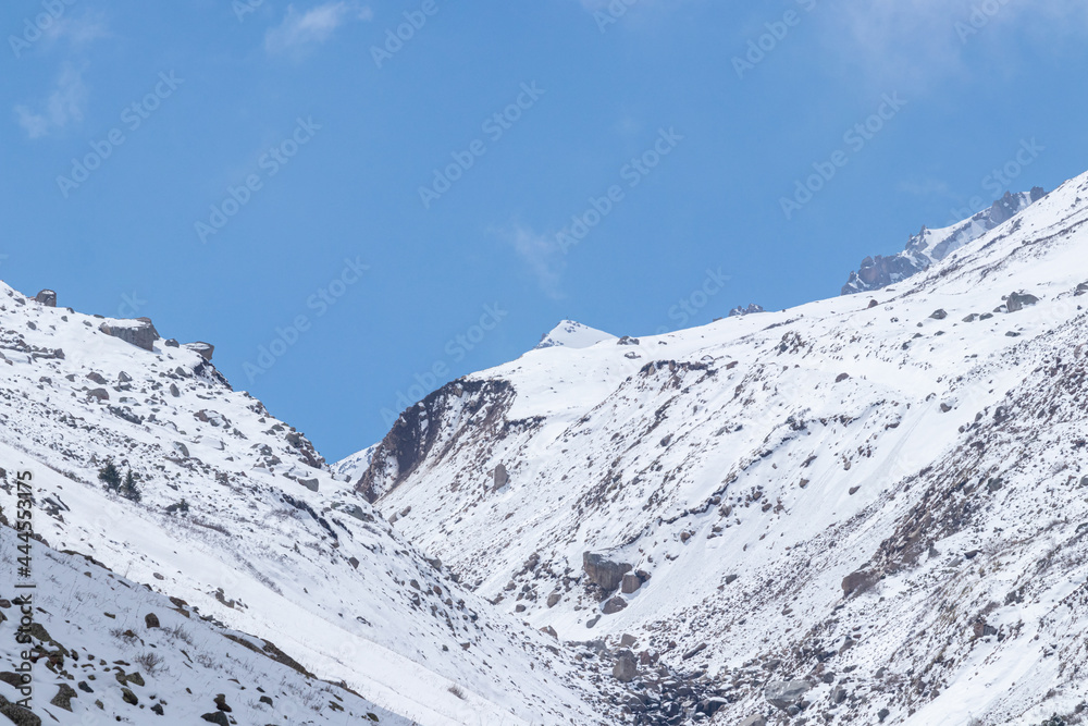 Mountain gorge with snowy slopes. Against the background of the blue sky and clouds