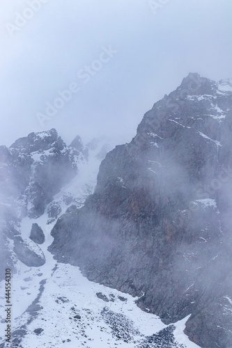 The mountain cliff is in fog, and there is snow at the foot