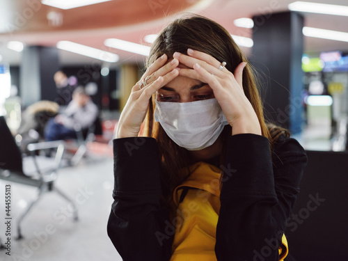 woman holding her head in a medical mask tiredness waiting for a flight airport