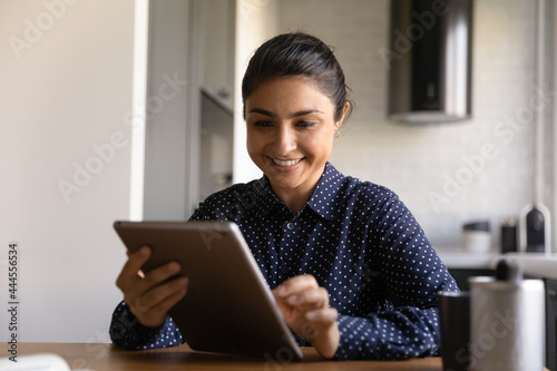 Happy Indian woman with tablet using app on computer for video call, shopping online, reading message and getting good news. Student watching webinar. Customer satisfied with Internet service work