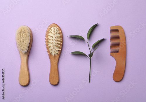 Wooden brushes and plant on violet background, flat lay. Conscious consumption