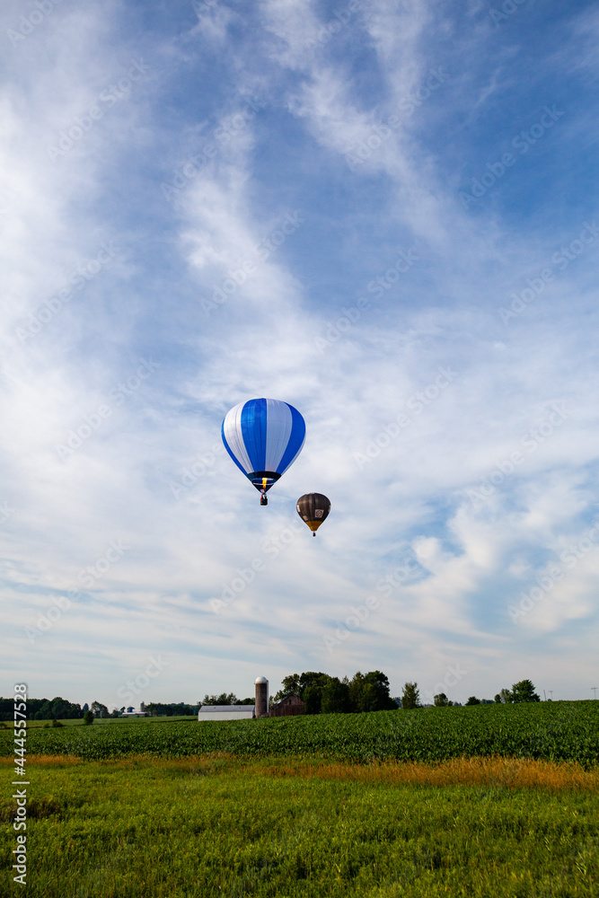Obraz premium Near Wausau, Wisconsin, USA, July 10, 2021, Taste N Glow Balloon Fest. Two hot air balloons in the the sky looking for a place to land in a famers field