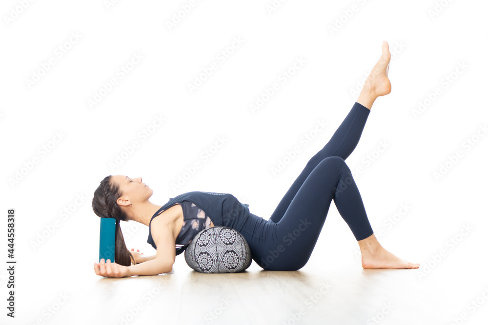 Restorative yoga with a bolster. Young sporty attractive woman in bright white yoga studio, lying on bolster cushion, stretching and relaxing during restorative yoga. Healthy active lifestyle Restorative yoga with a bolster. Young sporty attractive woman in bright white yoga studio, lying on bolster cushion, stretching and relaxing during restorative yoga. Healthy active lifestyle