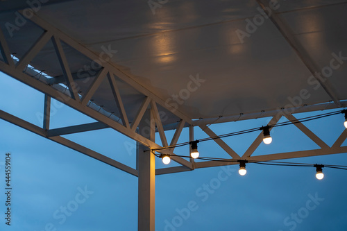 Textile visor on canopy with garland of energy saving lamps illuminating terrace of restaurant of night city
