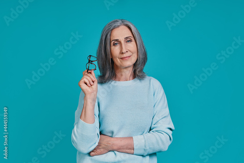 Mature beautiful woman looking at camera and smiling while standing against blue background