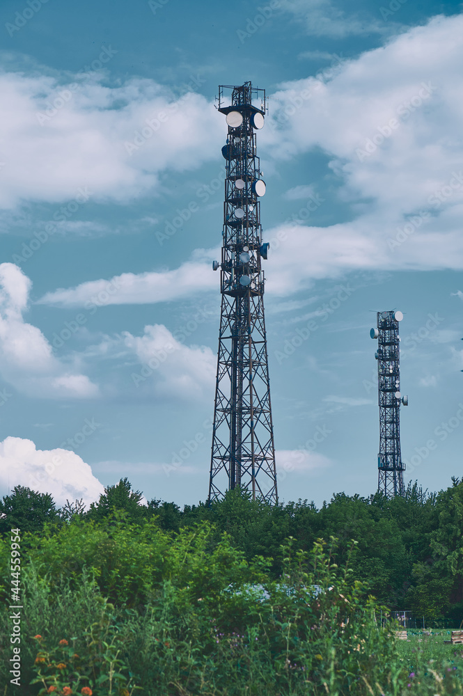 Obraz premium two telecommunication masts TV antennas wireless technology against blue sky over green hedges, cold color style