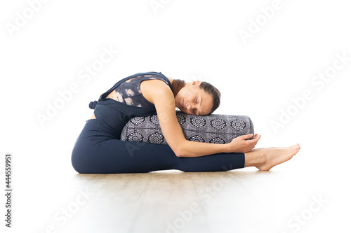 Restorative yoga with a bolster. Young sporty attractive woman in bright white yoga studio, lying on bolster cushion, stretching and relaxing during restorative yoga. Healthy active lifestyle photo