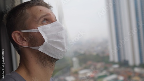 Obraz na plátně Face of a man in face mask standing by the window with his eyes closed as a sign