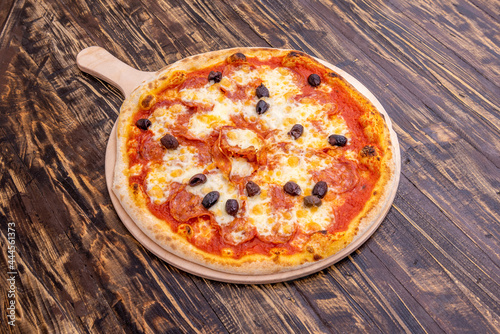Super diavola pizza with black olives, spicy pepperoni, mozzarella cheese and tomato on dark wooden table.
