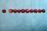 Ripe red apples hanging on light blue background, space for text