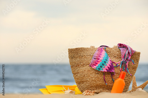 Bag and different beach objects on sand near sea, space for text