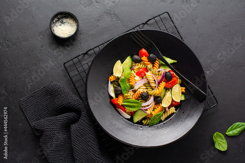 Whole grain pasta with vegetables on a white plate on black slate, stone or concrete background. Top view with copy space.