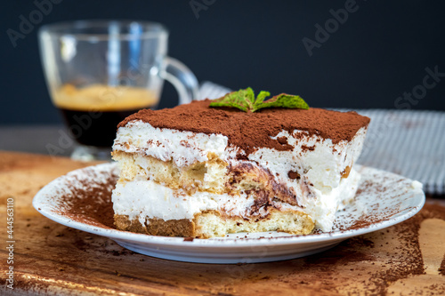 Slice of eaten traditional tiramisu cake with a cup of coffee in the background. Authentic gluten-free Italian layered dessert with ladyfinger biscuits, mascarpone cheese cream and cocoa powder. Side