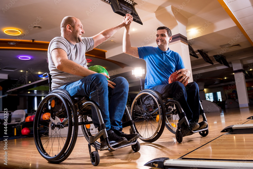 Obraz premium Two young disabled men in wheelchairs playing bowling in the club