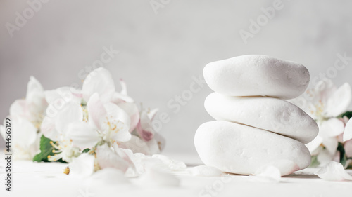 Stack of white pebble stones on light plaster surface, with apple flowers. Banner