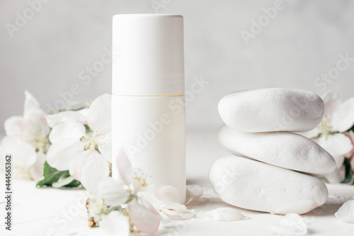 Antiperspirant roll-on deodorant near stack of white pebble stones on light plaster surface, with apple flowers