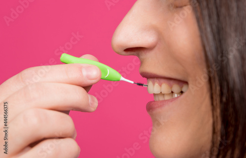 Beautiful happy young woman using interdental brush on the pink background