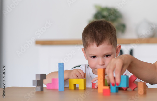 kid boy and mother playing educational toys at table at home. child's playing with colorful wooden bricks at the table.