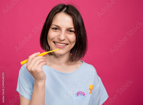 Beautiful happy young woman with single tufted toothbrush on blank pink background