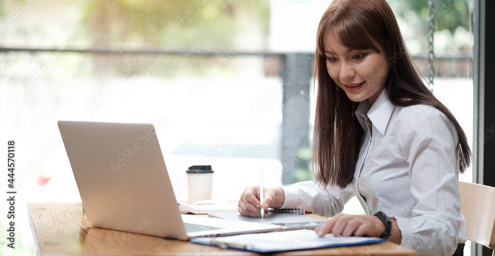 A young, cheerful girl in a white shirt smiles, smiling toothily writing down notes holding training for students to be executives at laptop desktop table A young, cheerful girl in a white shirt smiles, smiling toothily writing down notes holding training for students to be executives at laptop desktop table