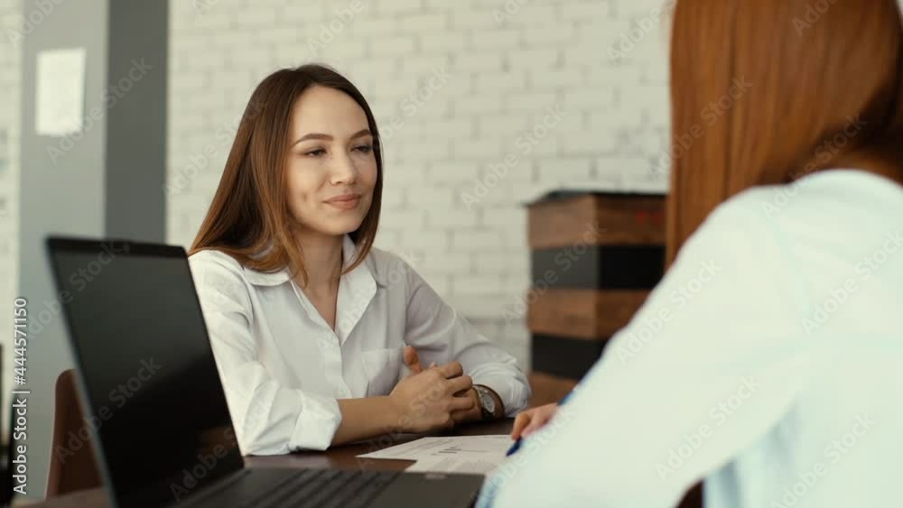 Close-up rear view of female applicant during job interview talking to young woman employers. Businesswoman sitting at desk interviewing lady candidate in modern office. Shooting in slow motion. Close-up rear view of female applicant during job interview talking to young woman employers. Businesswoman sitting at desk interviewing lady candidate in modern office. Shooting in slow motion.
