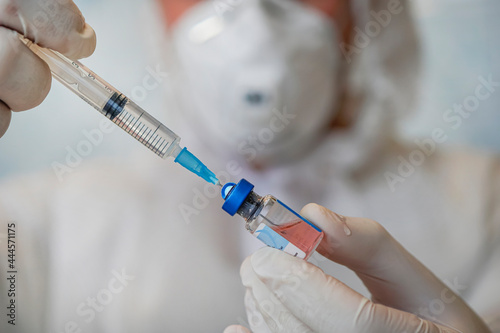 bottle of vaccine close-up in the hand of a doctor with white gloves on a blue background. photo