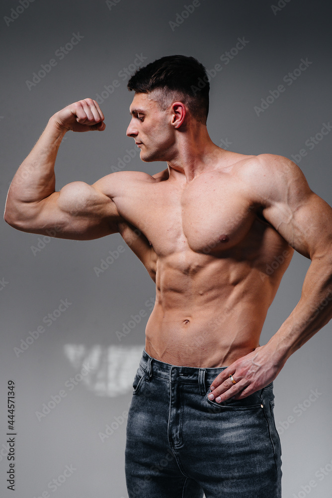 Obraz premium A young sexy athlete with perfect abs poses in the studio topless in jeans on the background. Healthy lifestyle, proper nutrition, training programs and nutrition for weight loss.