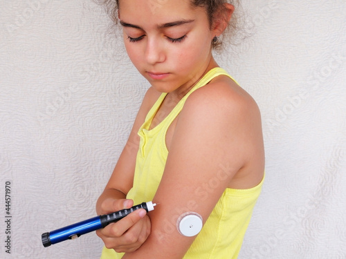Girl stands and injects insulin from insulin pen in arm. On the arm is also placed white sensor for continuous glucose monitoring in blood - CGM. Diabetes type 1. Insulin dependent photo
