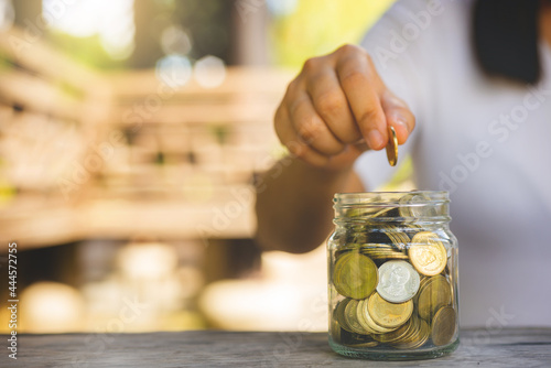 Slika na platnu hand of business woman put golden coin on jar with green blur nature background