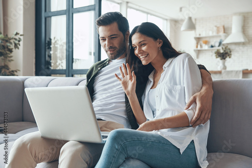 Beautiful young couple drinking coffee and looking on the laptop while sitting on the sofa at home