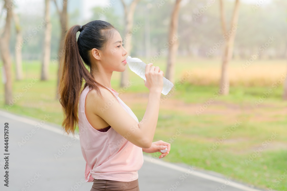 Beautiful Asian woman taking a water break after exercising in the park every morning Beautiful Asian woman taking a water break after exercising in the park every morning