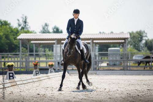 portrait of man rider and black stallion eventing horse trotting leg-yield during equestrian dressage competition in summer